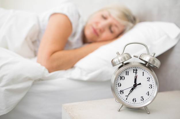 Mujer durmiendo en la cama con reloj despertador en primer plano en el dormitorio