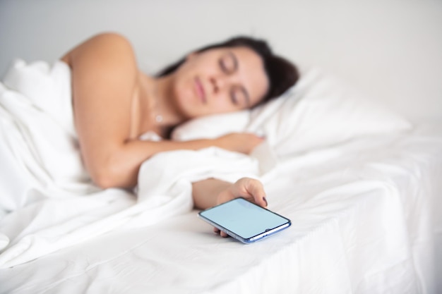 Mujer durmiendo en la cama con el teléfono en la mano