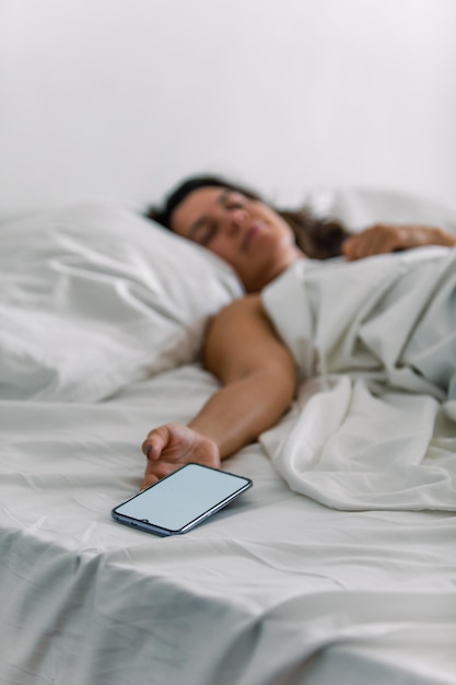 Mujer durmiendo en la cama con el teléfono en la mano