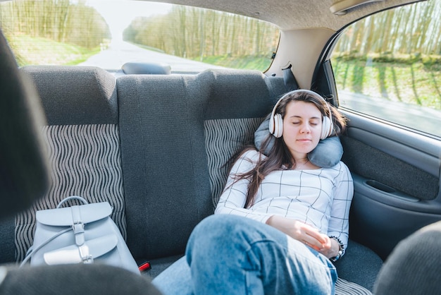 Mujer durmiendo en el coche en el asiento trasero y escuchando música en auriculares. concepto de viaje