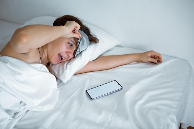 Mujer durmiendo en un smartphone con antifaz para dormir cerca de ella