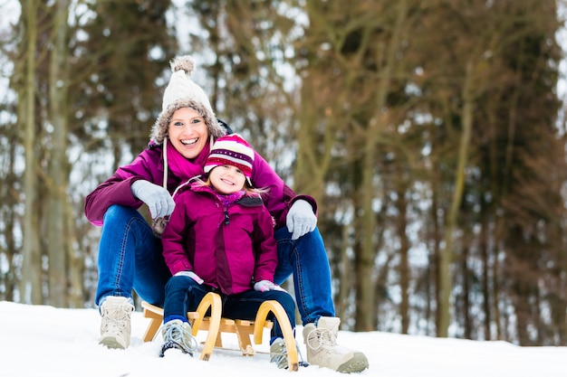 Mujer e hija en trineo en invierno