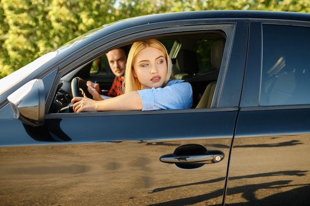 Mujer e instructor mirando por la ventanilla del coche, escuela de conducción. Hombre enseñando a la señora a conducir un vehículo. Educación sobre licencias de conducir