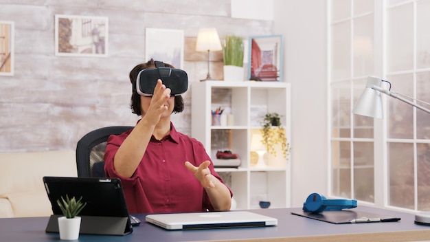 Mujer de edad avanzada con gafas de realidad virtual en la sala de estar. Anciano sentado en el sofá en el fondo.