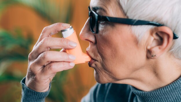 Foto mujer de edad avanzada que utiliza inhalador de asma con tubo de extensión