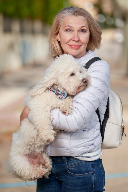 Mujer de edad caminando con perro blanco esponjoso en la ciudad de verano