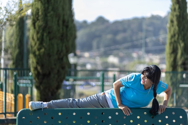 Foto mujer de edad mexicana que se extiende en un banco del parque, formación urbana