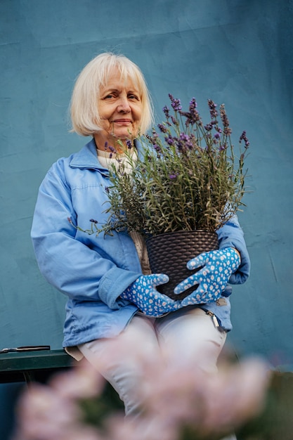 mujer de edad positiva con flores de lavanda en macetas. sonriente anciana en ropa casual