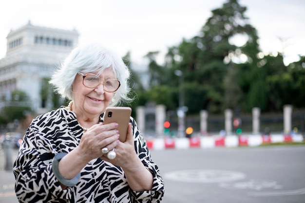 Mujer de edad sosteniendo su teléfono celular en la calle