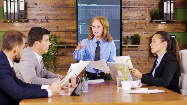 Mujer ejecutiva caucásica dando a su joven equipo nuevos gráficos para estudiar. Reunión de negocios importante.