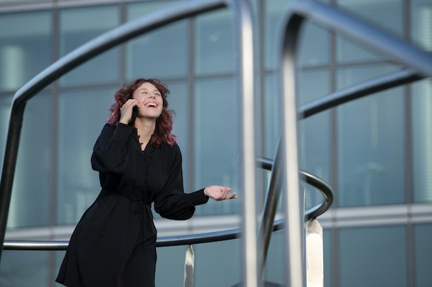 Mujer ejecutiva felizmente hablando por teléfono celular al aire libre en un ambiente de negocios