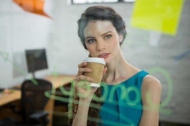 Mujer ejecutiva pensativa mirando notas adhesivas mientras toma café