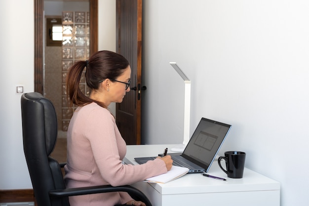 Mujer ejecutiva que trabaja desde casa, sentado en el escritorio con ordenador portátil, mirando a la cámara. Nuevo normal - espacio de copia