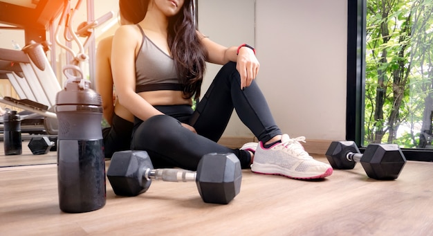 Mujer ejercicio entrenamiento en gimnasio fitness romper relajarse después de entrenar deporte con mancuernas y botella de agua.