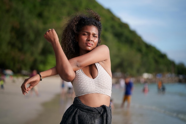 Mujer ejercita y estira los músculos antes de hacer ejercicio al aire libre Retrato sexy dama africana asiática preparándose para hacer ejercicio en la playa