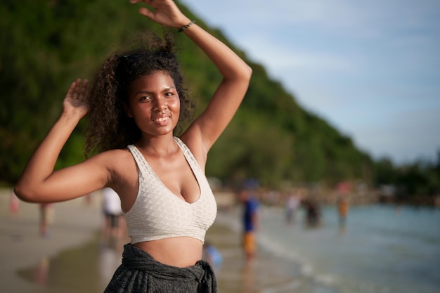 Mujer ejercita y estira los músculos antes de hacer ejercicio al aire libre Retrato sexy dama africana asiática preparándose para hacer ejercicio en la playa