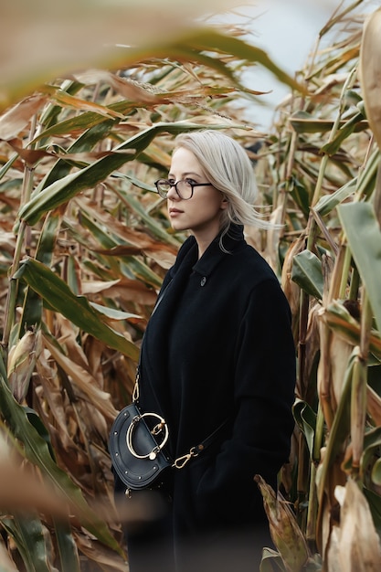 Mujer elegante en abrigo negro en campo de maíz de otoño