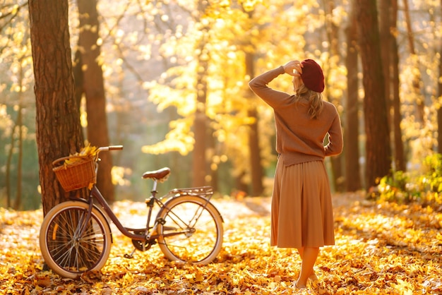 Mujer elegante con bicicleta disfrutando del clima otoñal en el parque Mujer hermosa en el bosque de otoño