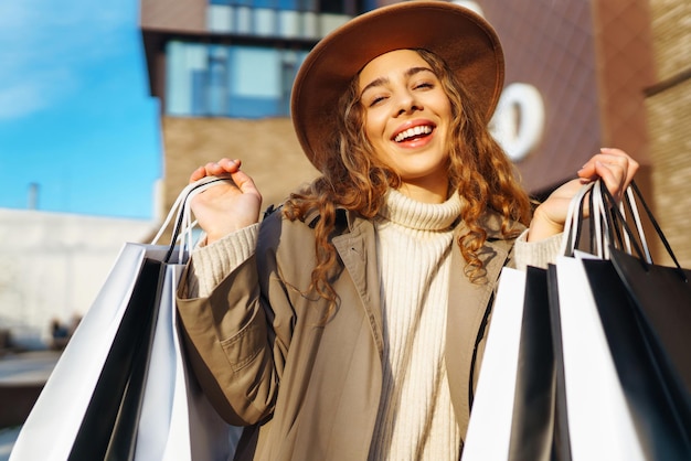 Mujer elegante con bolsas de compras camina por las calles de la ciudad Consumerismo concepto de estilo de vida de compras