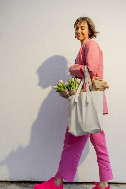 Mujer elegante con bolso de mano y flores en el fondo