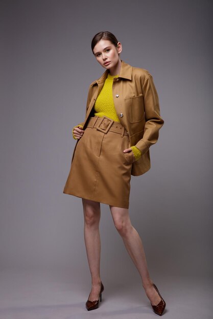 Mujer elegante en una bonita chaqueta de arena beige marrón falda suéter amarillo mostaza sobre fondo gris