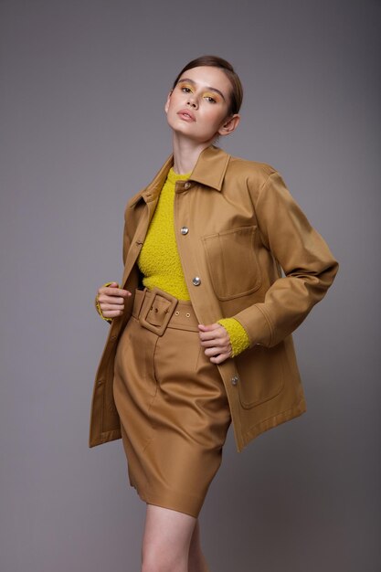 Mujer elegante en una bonita chaqueta de arena beige marrón falda suéter amarillo mostaza sobre fondo gris