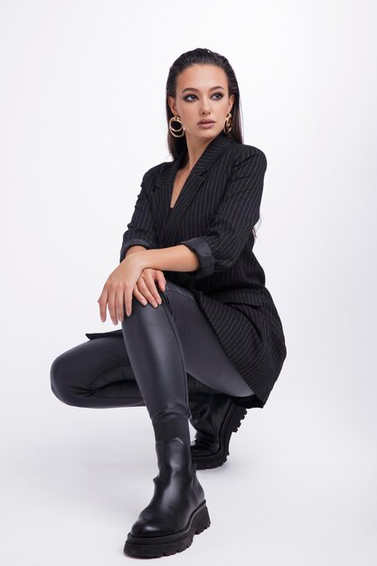 mujer elegante con bonita chaqueta negra, pantalones de cuero, botas de fondo blanco.