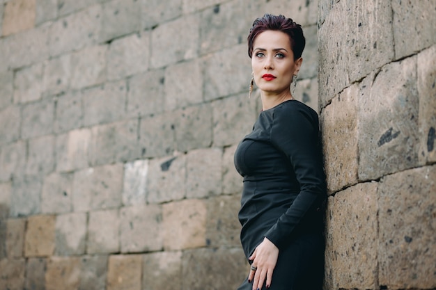 Mujer elegante y bonita con vestido negro apoyado en el antiguo castillo