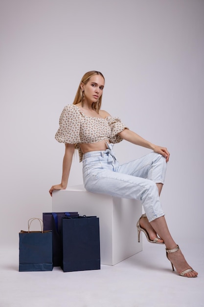 mujer elegante con bonitos jeans azules, top beige, bolsas de compras con fondo blanco