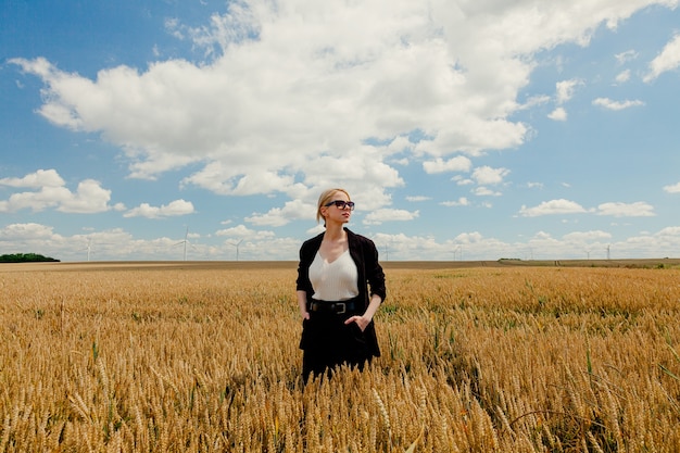 Mujer elegante con cabello rubio posando en ropa formal en campo de trigo