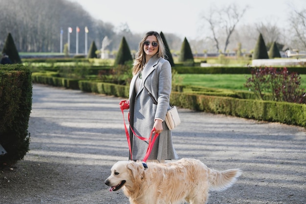 Mujer elegante caminando con un labrador con correa en un parque