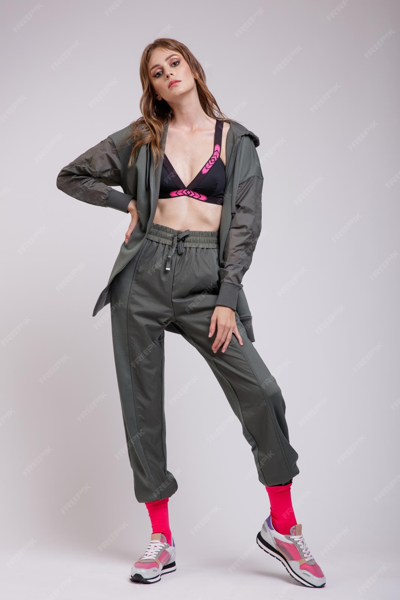 Mujer elegante en chaqueta de chándal verde pantalones deportivos sujetador zapatillas rosa calcetines sobre fondo | Foto Premium