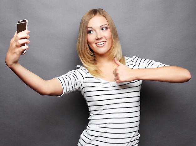 Mujer elegante haciendo foto selfie en smartphone sobre backg gris