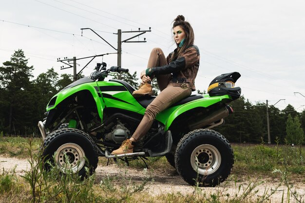 Mujer elegante y hermosa y el ATV en el camino forestal