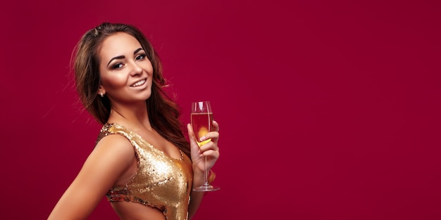 Mujer elegante joven en maquillaje de noche vestido de brillo dorado sosteniendo una copa de champán y celebratin ...