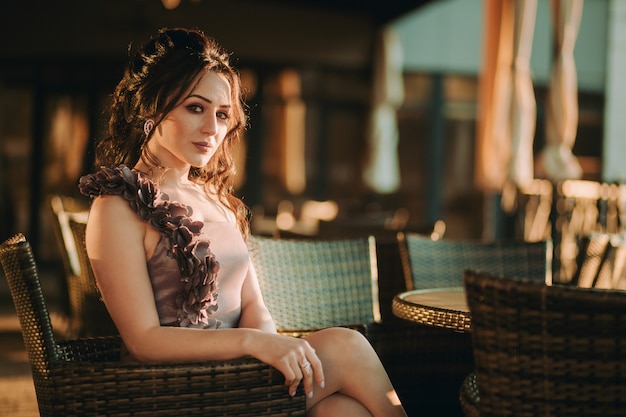 Mujer elegante joven sentada en el café de la calle solo y posando para la cámara en la noche