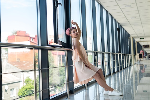 Mujer elegante y joven con vestido rosa posando dentro de un largo pasillo