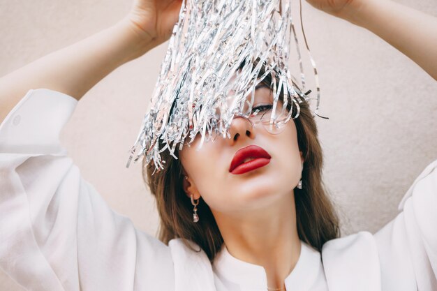 Mujer elegante con labios rojos en blusa blanca y tiras de oropel plateado de metal plateado