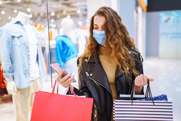 Mujer elegante con máscara médica protectora con bolsa de compras usando su teléfono Estilo de moda Blackfriday