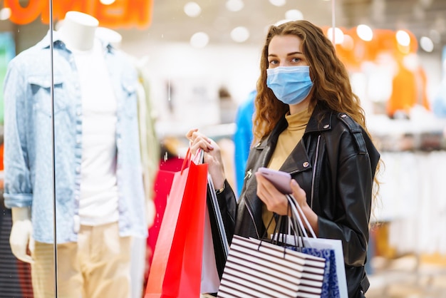 Mujer elegante con máscara médica protectora con bolsas de compras usando su teléfono Estilo de moda