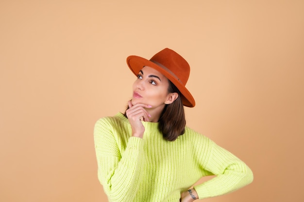 Mujer elegante de moda en pleno crecimiento en pantalones, un suéter y un sombrero mira pensativamente a un lado, sonriendo