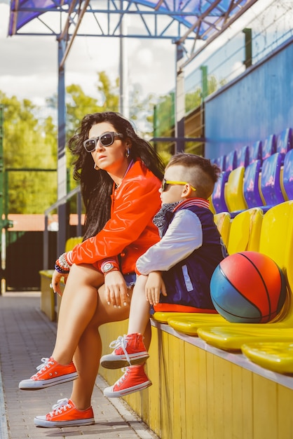 Mujer elegante y niño posando en la cancha de baloncesto