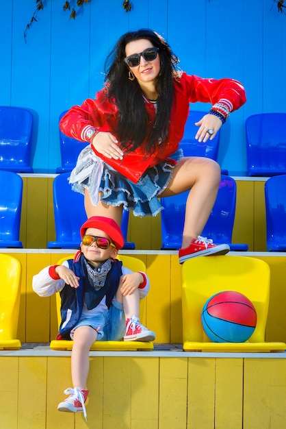 Mujer elegante y niño posando en la cancha de baloncesto.