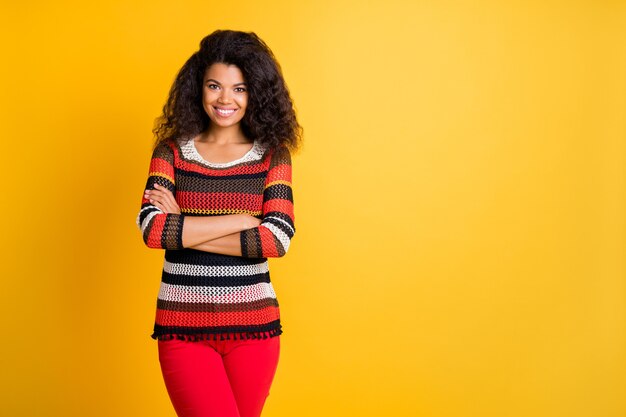 Mujer elegante con peinado afro posando contra la pared naranja