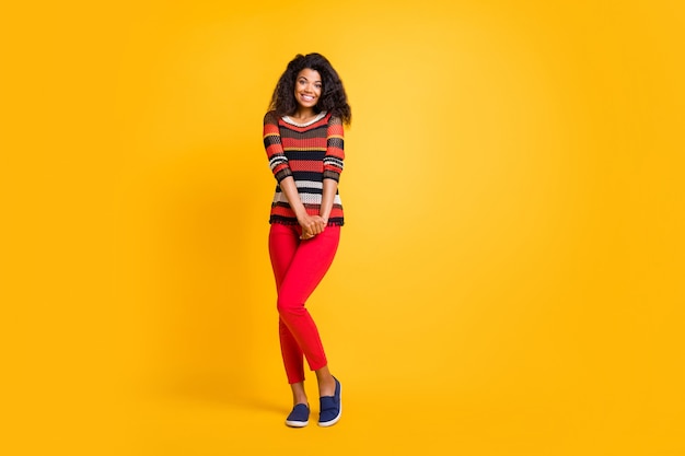 Mujer elegante con peinado afro posando contra la pared naranja