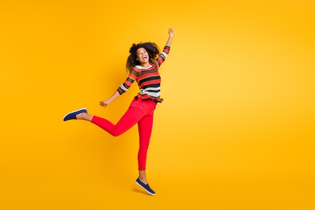 Mujer elegante con peinado afro posando contra la pared naranja