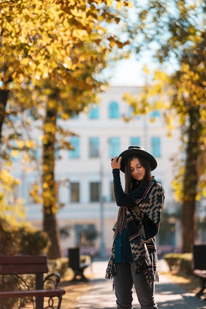 Mujer elegante con poncho y sombrero disfruta del parque de otoño