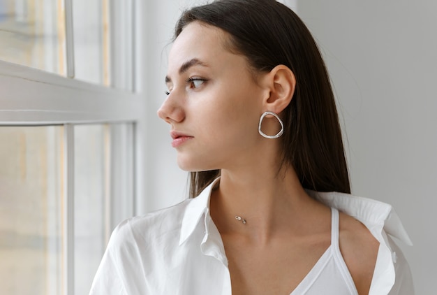 Mujer elegante romántica joven blanca en camisa blanca junto a la ventana