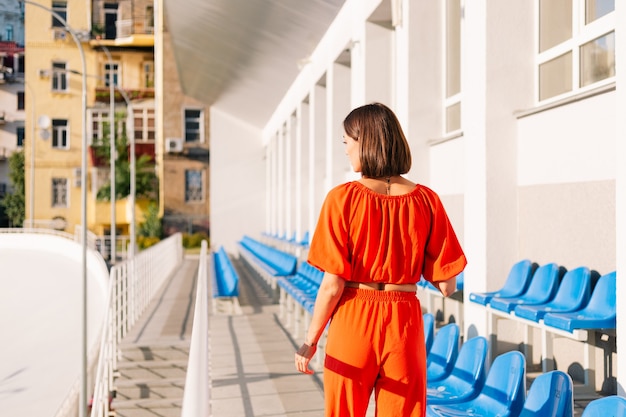 Mujer elegante en ropa naranja al atardecer en el estadio de pista para bicicletas posando