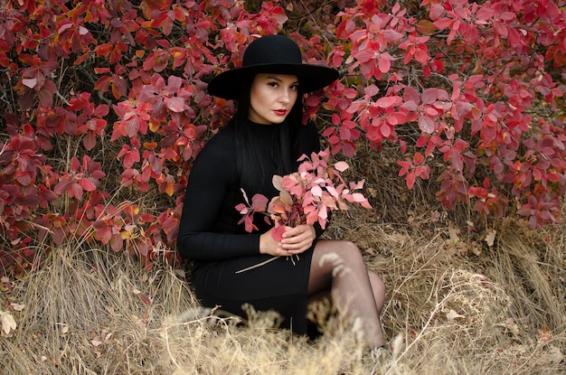 Mujer elegante se sienta en un parque de otoño contra el fondo de hojas rojas